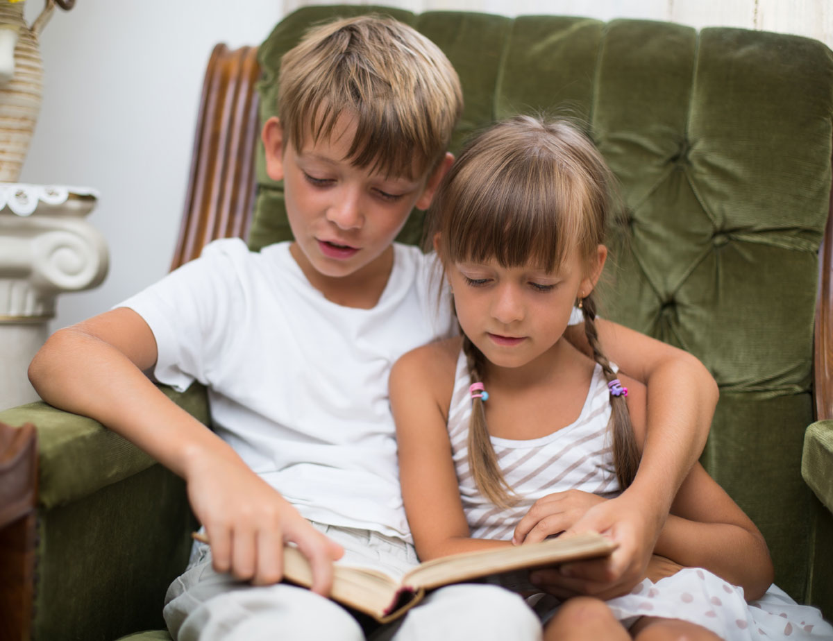 A young brother reading to younger sister